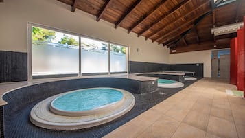 Una amplia piscina interior con varios jacuzzis, suelo de baldosas y techo de madera.