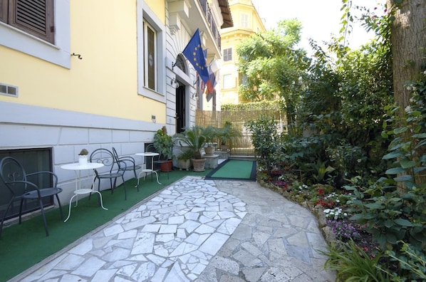 A courtyard with outdoor seating, a stone pathway, and a variety of plants and flowers. - Hotel Silva (Rome)