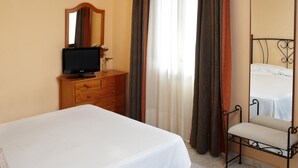 Hotellihuone, jossa on sänky, puinen lipasto, jossa on televisio, tuoli ja suuri peili.