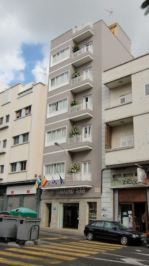 Ein mehrstöckiges Hotel mit Balkonen, einem gut sichtbaren Eingang und einem geparkten Auto davor.