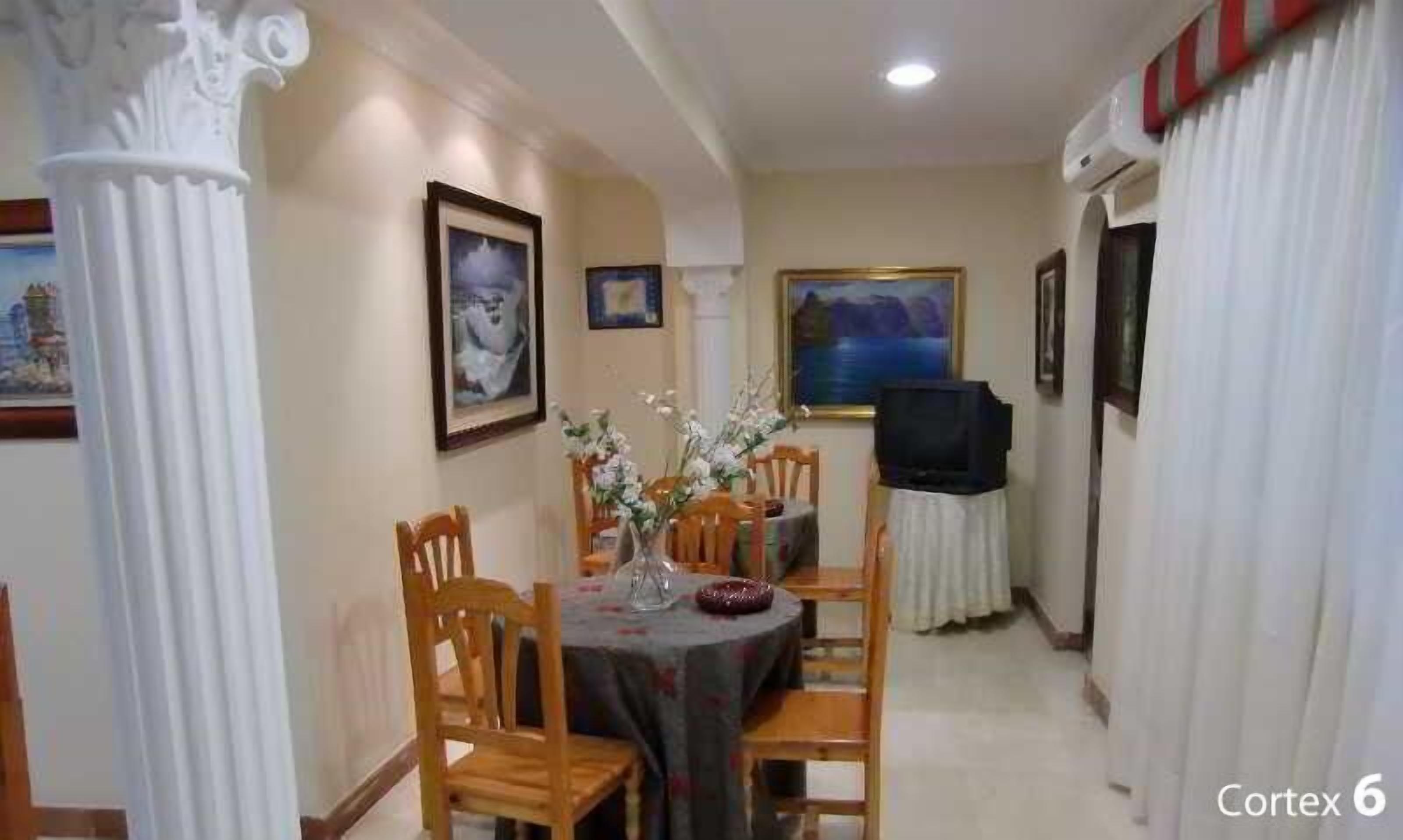 A dining area with a round table, chairs, a vase with flowers, and framed pictures on the walls.