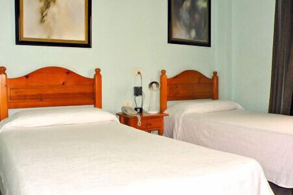 A room with two wooden beds, a nightstand with a lamp, and a painting on the wall.