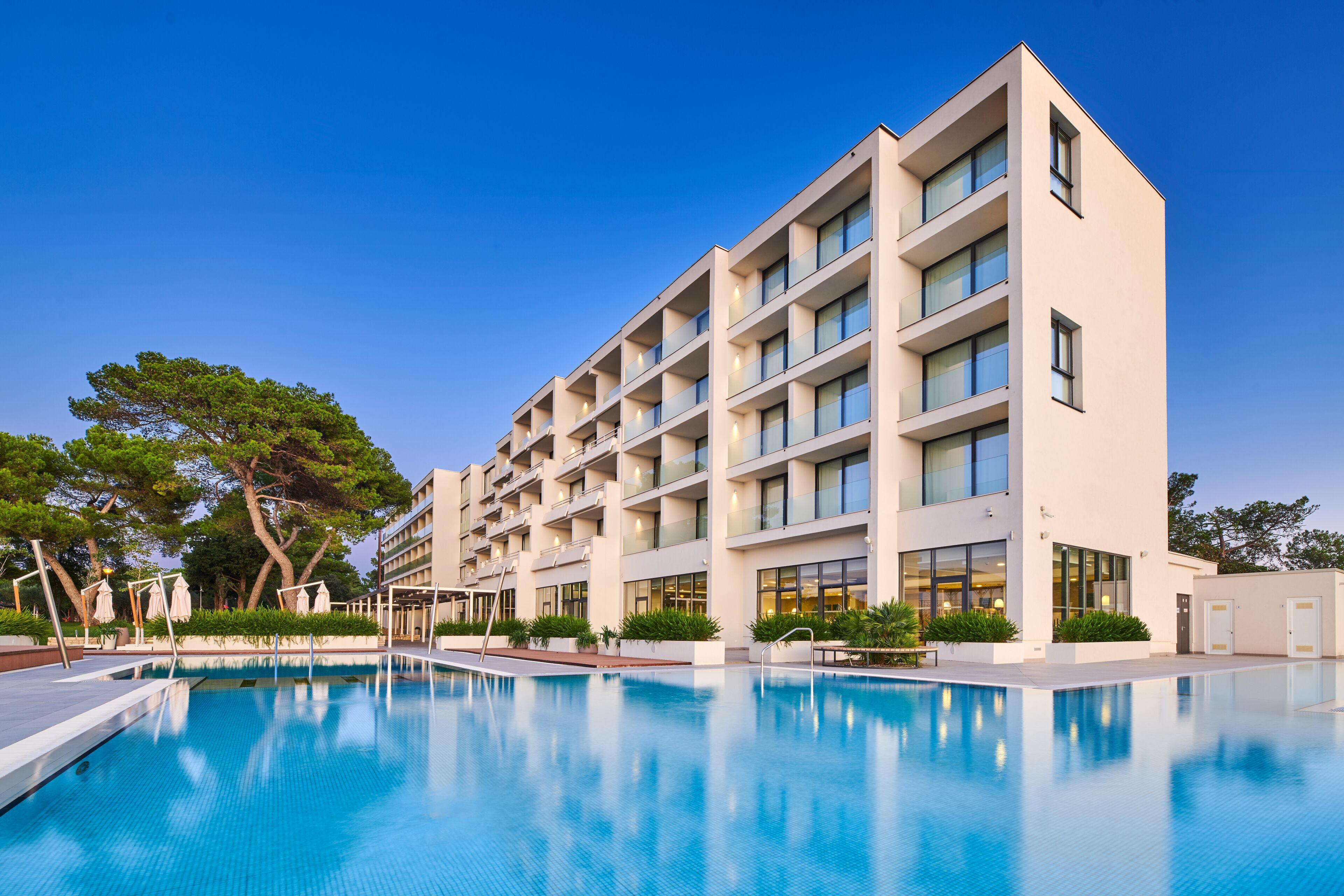 Ein modernes Hotel mit Schwimmbad, mehreren Balkonen und blauem Himmel.