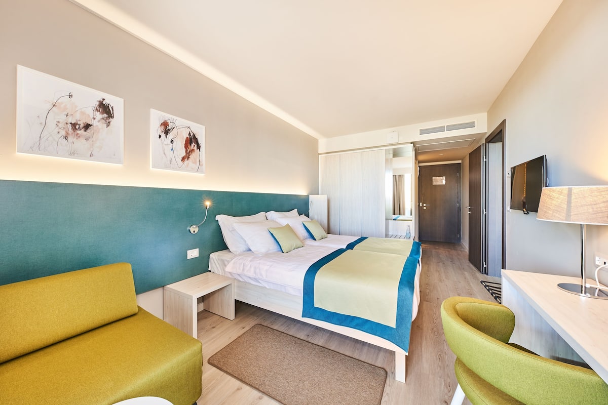 A modern hotel room with a bed, a desk, and a seating area.