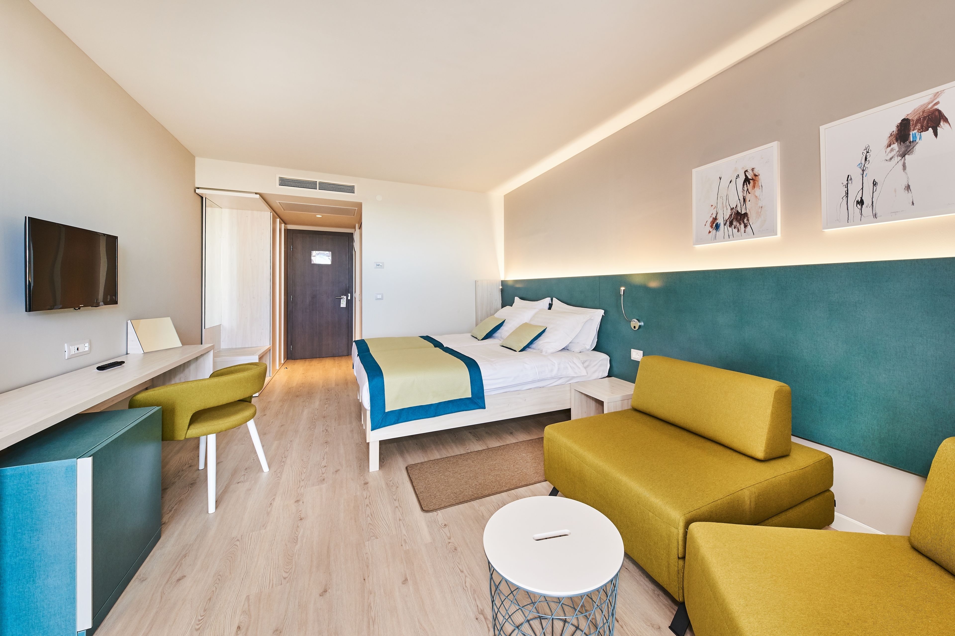 A modern hotel room with a bed, a desk, a chair, and a sofa.