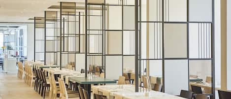 A modern dining area with long tables and chairs, partitioned by black and white panels.