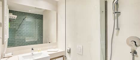 A modern bathroom with a glass-enclosed shower, a white sink with a mirror above it, and a green-tiled wall.