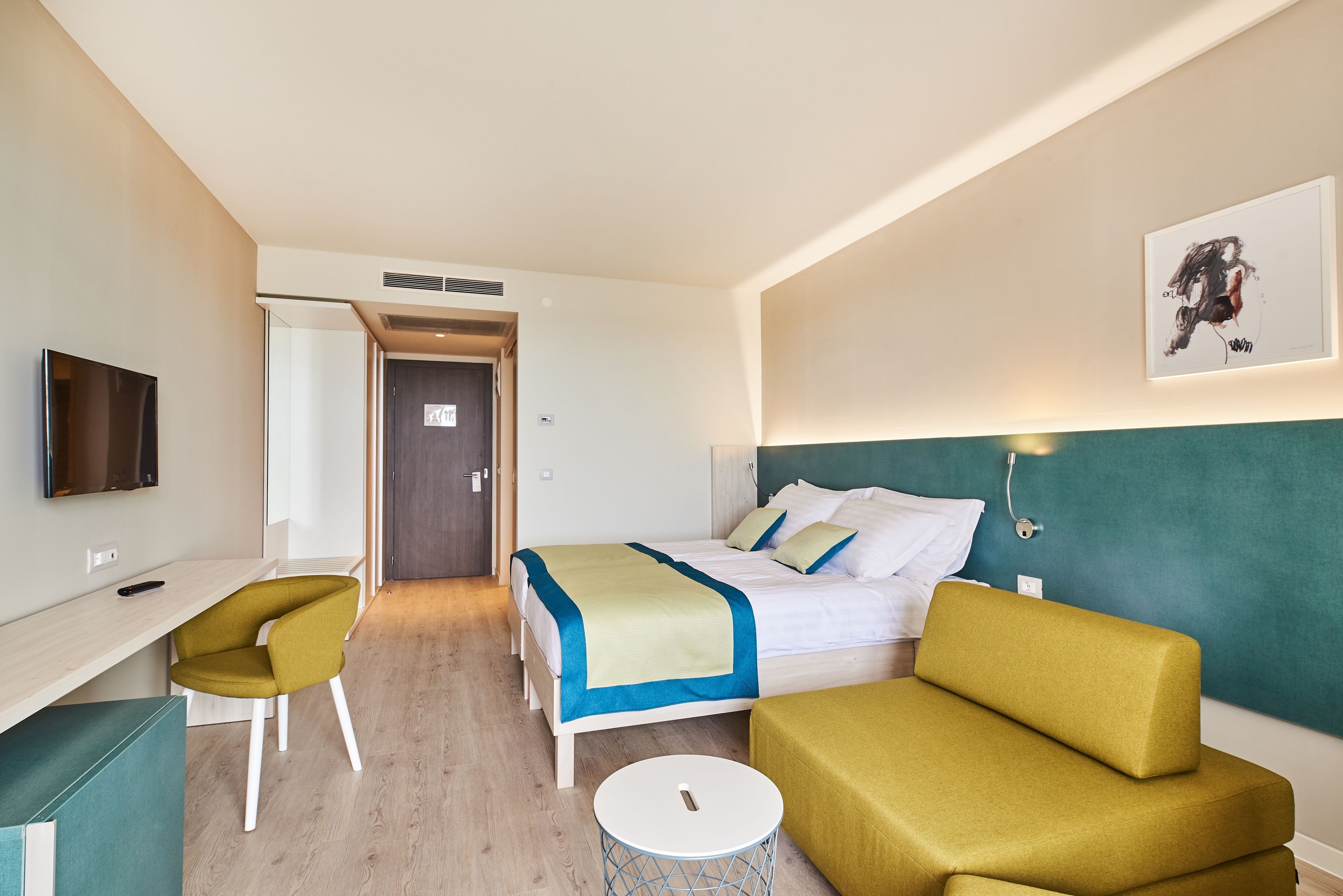 Une chambre d’hôtel avec un lit, un bureau, une chaise, une petite table ronde et un téléviseur.