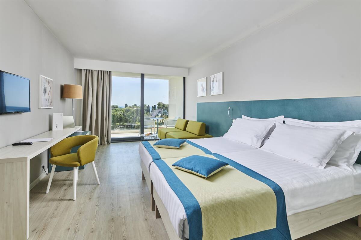 A hotel room with a large bed, a desk, a chair, and a view of the outdoors.