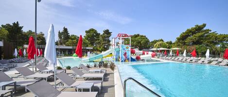 A pool area with lounge chairs, umbrellas, and a water slide.