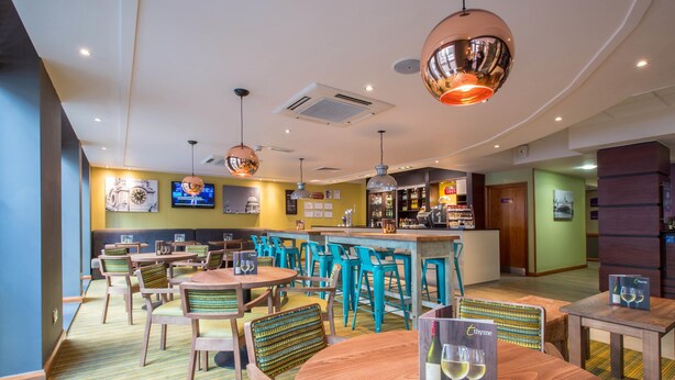 Een restaurant met houten tafels en stoelen, een bar en een televisiescherm.