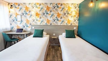 A hotel room with two single beds, a desk with a laptop, and a chair.