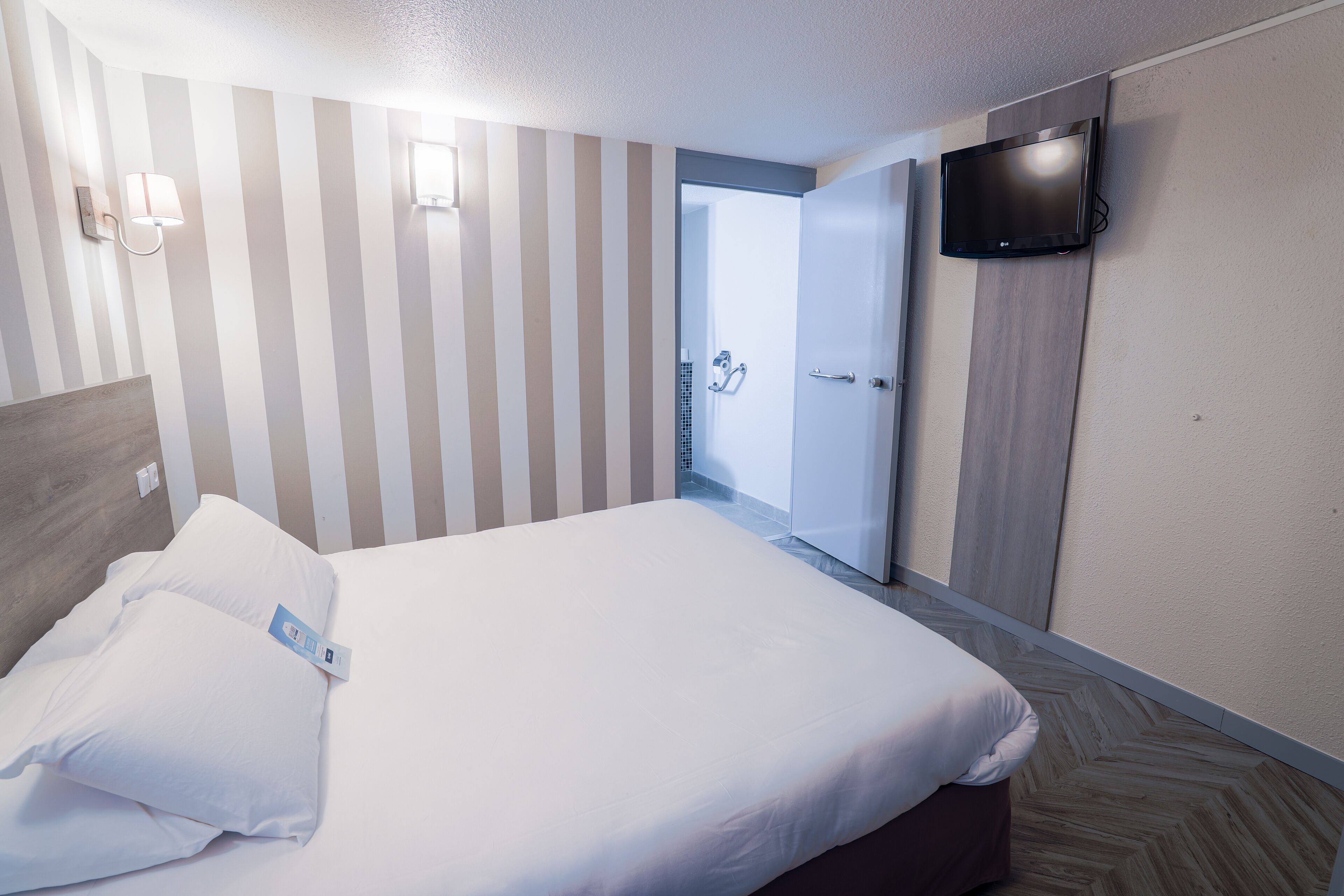 Una habitación de hotel con una cama, un televisor montado en la pared y una puerta que da al baño.