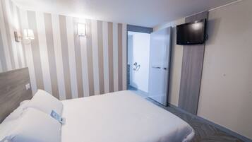 Una habitación de hotel con una cama, un televisor montado en la pared y una puerta que da al baño.