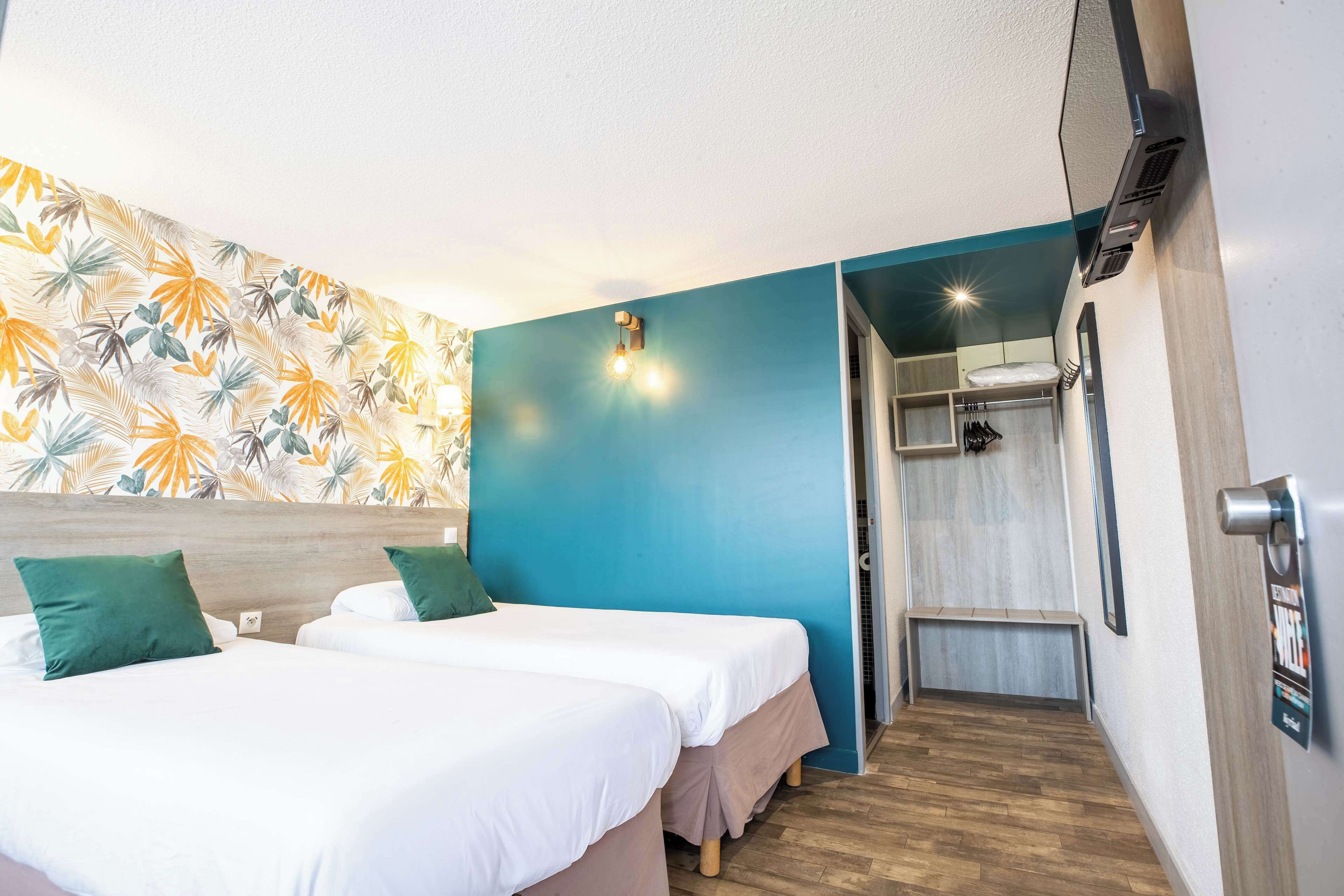 Habitación de hotel con dos camas, zona de ducha y un diseño de hojas tropicales en la pared.