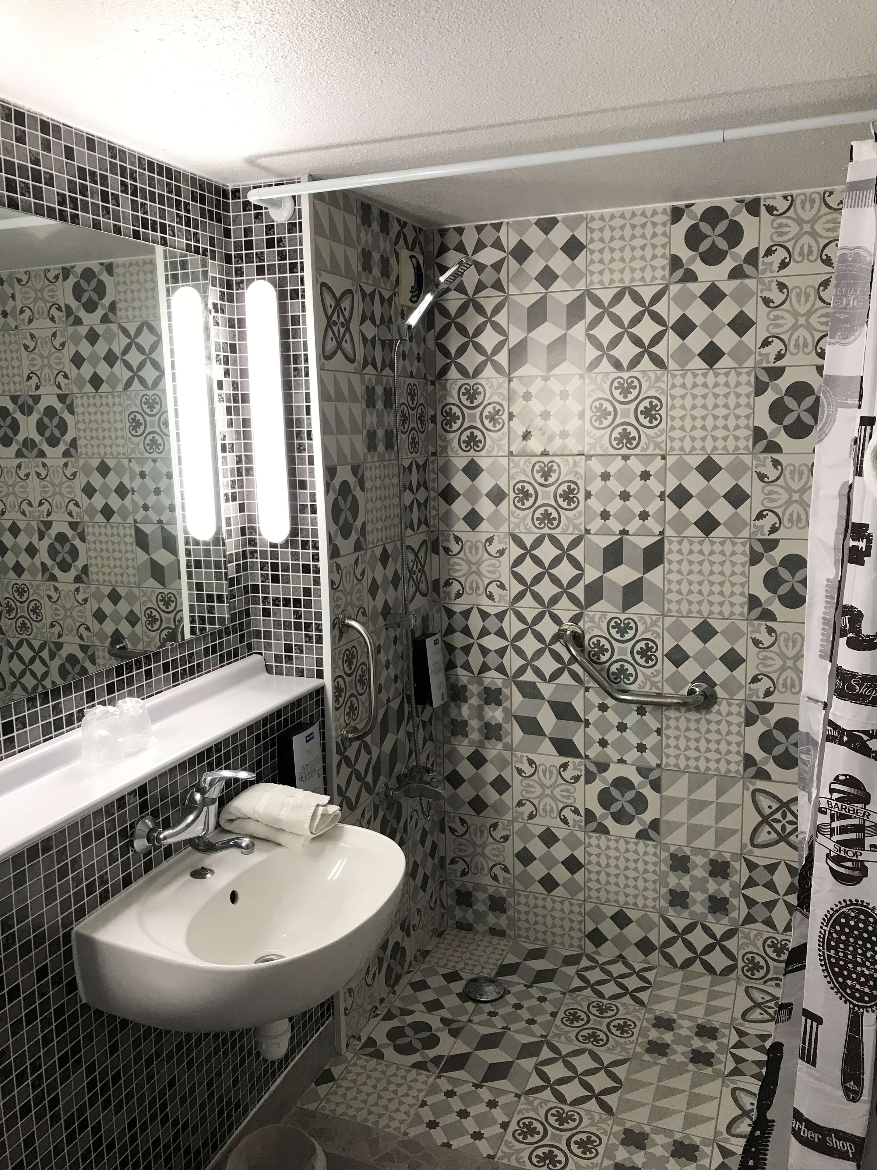 Un baño con lavamanos blanco, un espejo y una ducha con azulejos decorados.