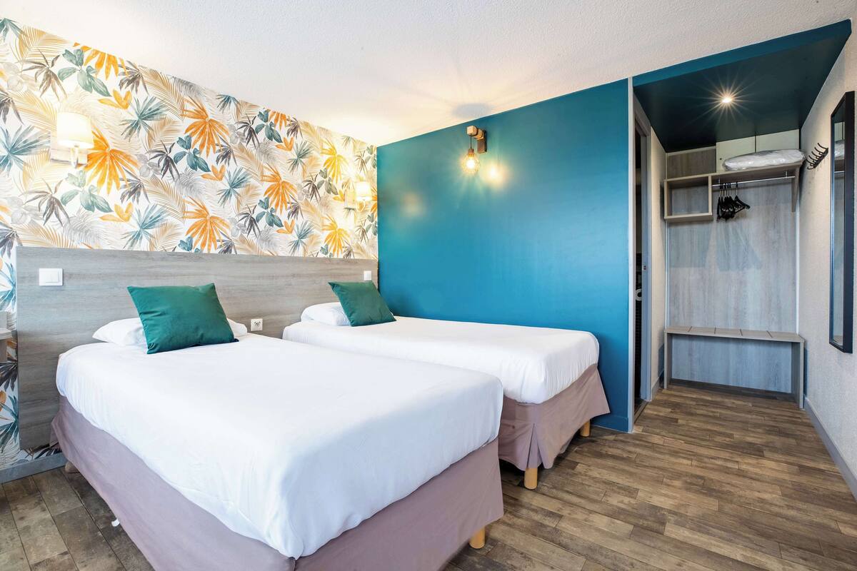 A room with two beds, a shower area, and a wall with a tropical leaf pattern.