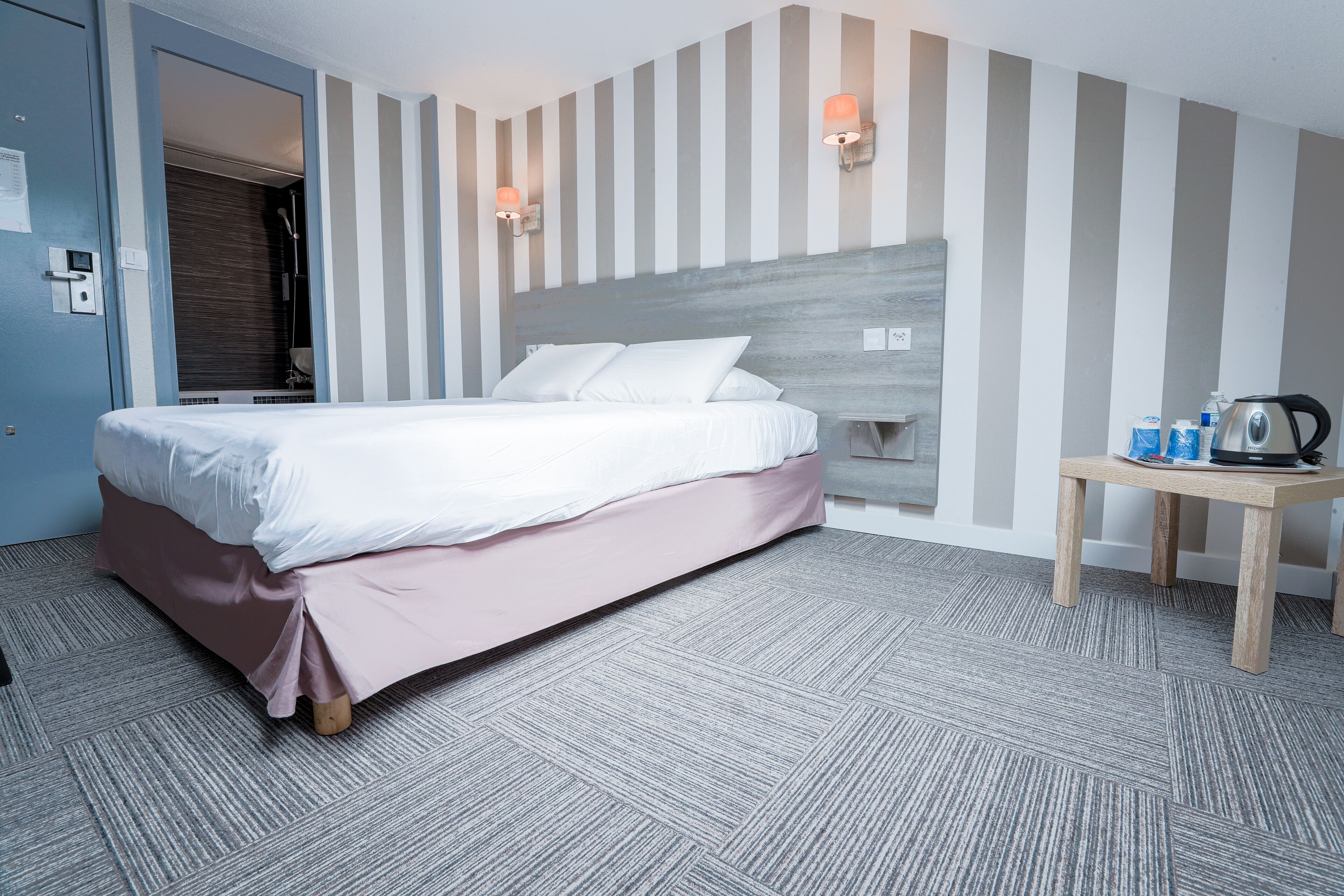 Een hotelkamer met een bed, een houten nachtkastje en een gestreepte wand.