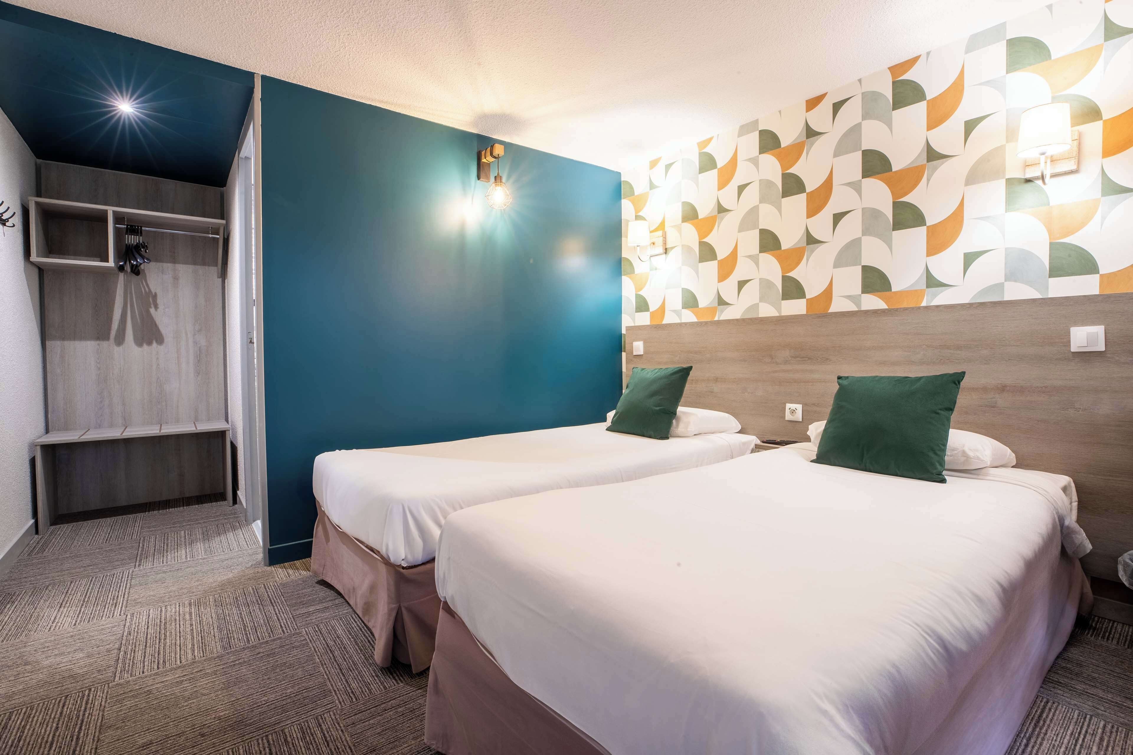 A hotel room with two beds, a wooden headboard, a patterned wall, and a built-in bench with hooks.