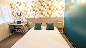 A hotel room with a bed, two green pillows, a desk with a laptop, and a patterned wall.