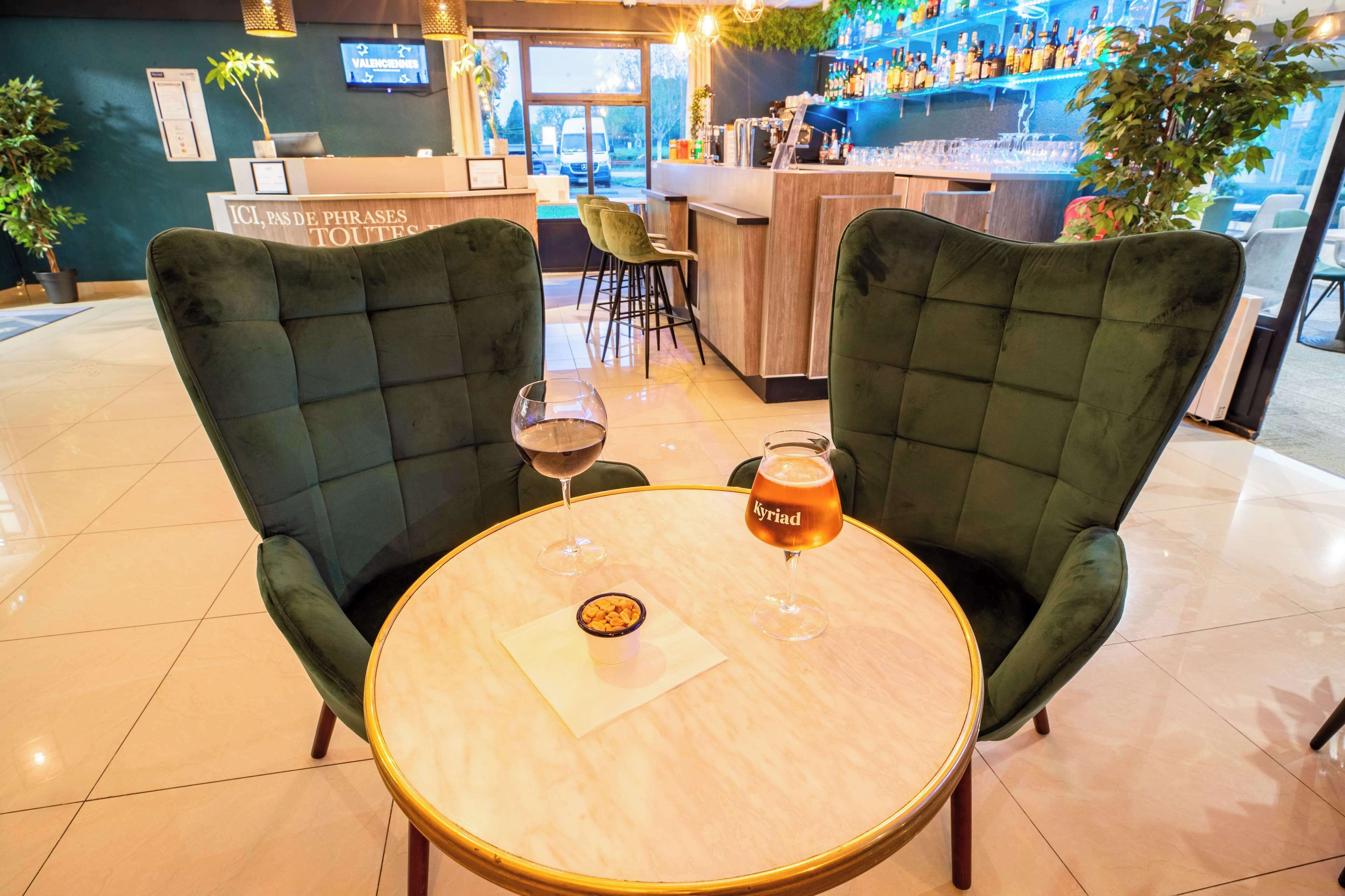 Zona de bar amb dues cadires tapissades de verd al voltant d'un taula rodona, una copa de cervesa i un got de vi.