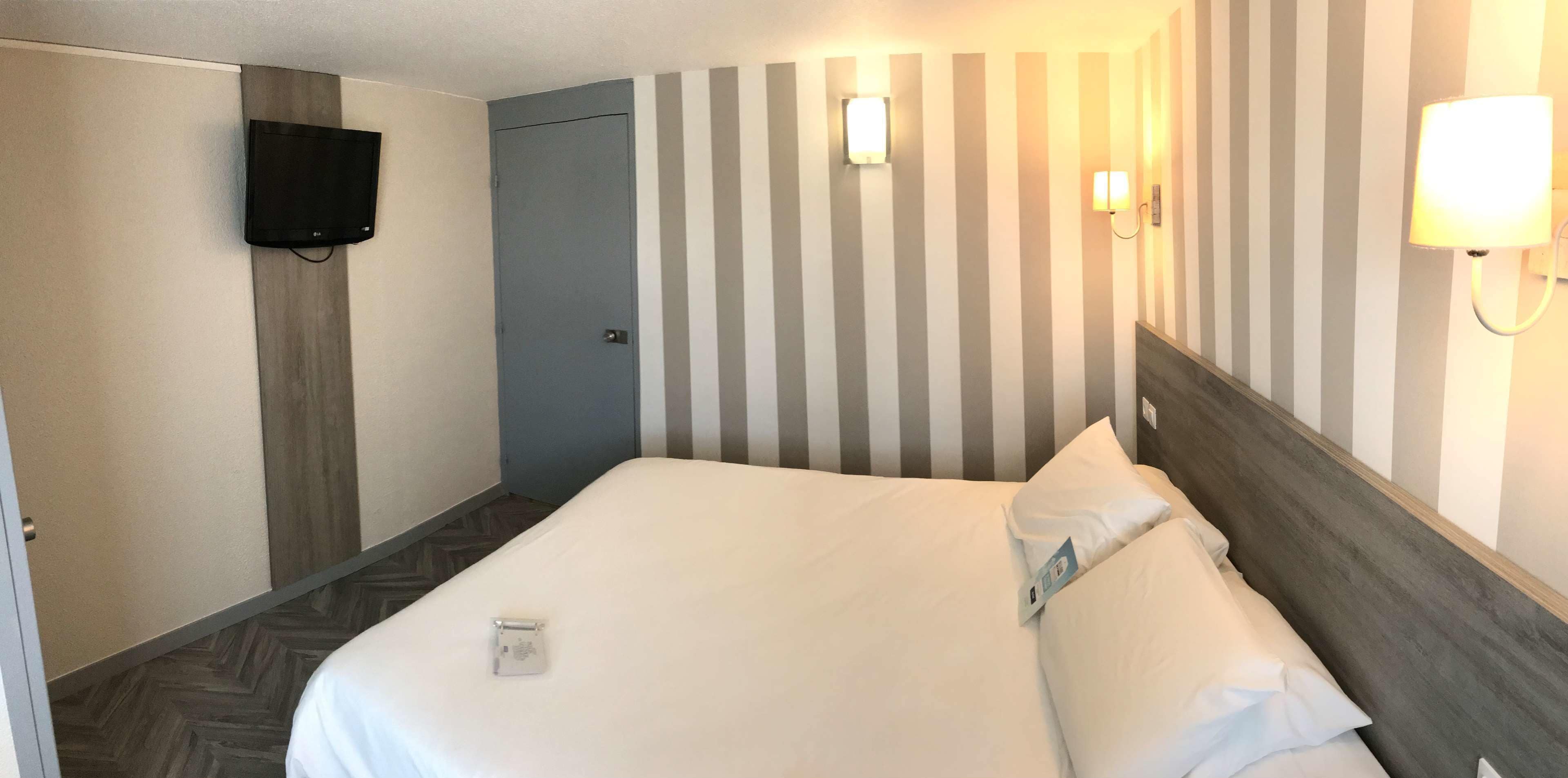 Una habitación de hotel con una cama, un televisor montado en la pared y una puerta.