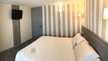 Una habitación de hotel con una cama, un televisor montado en la pared y una puerta.