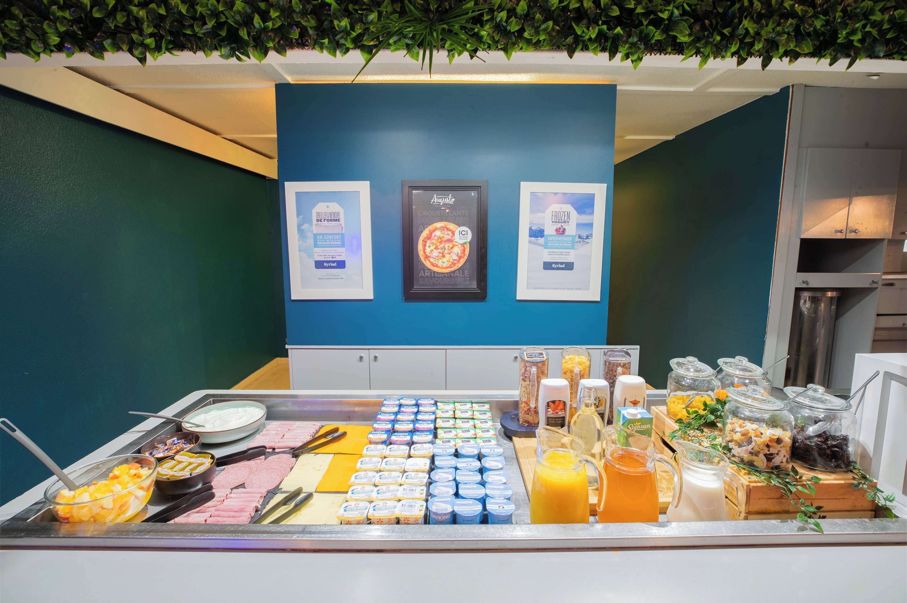 A breakfast buffet with various food items and beverages, framed certificates on the wall, and a kitchen area in the background.