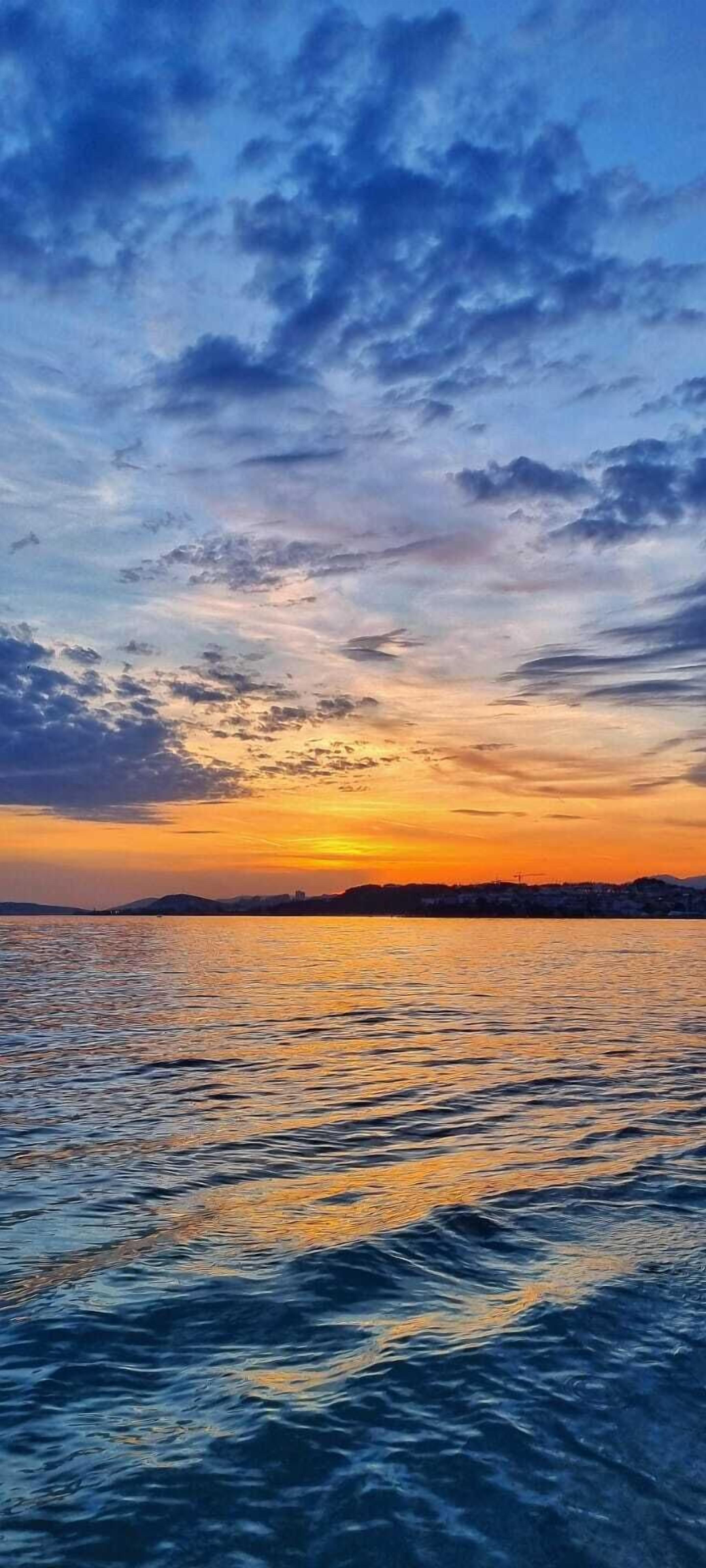 Een zonsondergang boven een wateroppervlak met een verre kustlijn.