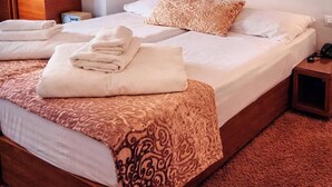 Una cama bien hecha con una colcha estampada y almohadas, una mesita de noche con lámpara, y un suelo cubierto de moqueta roja.