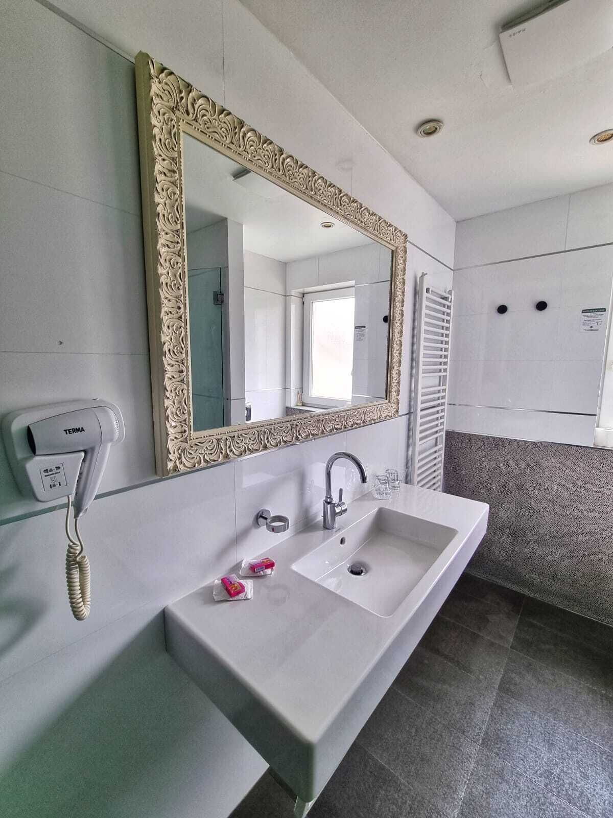 A bathroom with a white sink, a mirror with an ornate frame, a towel rack, and a wall-mounted telephone.