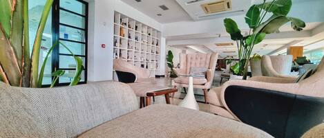 A modern living room with a sofa, armchairs, and a coffee table. There is a bookshelf filled with books and decorative items.