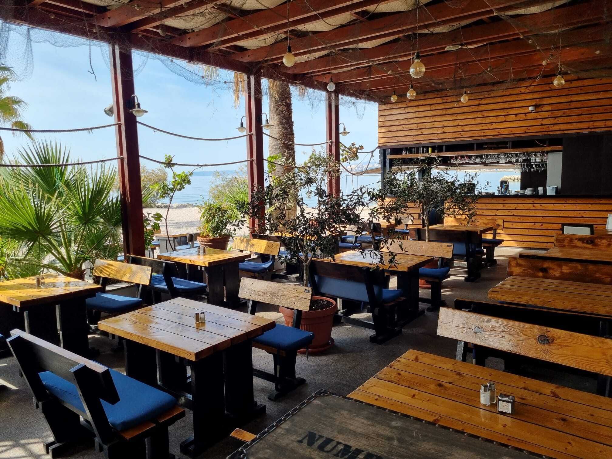 Un café en plein air avec des tables en bois et des chaises bleues dotées de coussins, offrant une vue sur la plage.