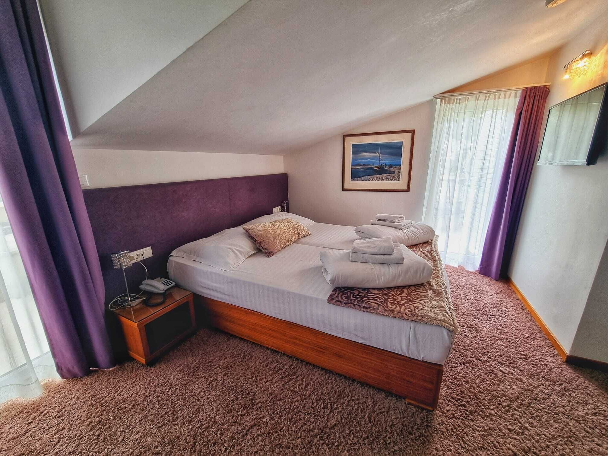 A bedroom with a bed, a nightstand, a painting, and a window with curtains.