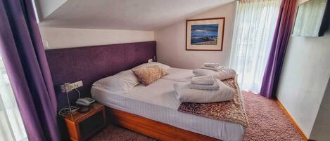 A bedroom with a bed, a nightstand, a painting, and a window with curtains.
