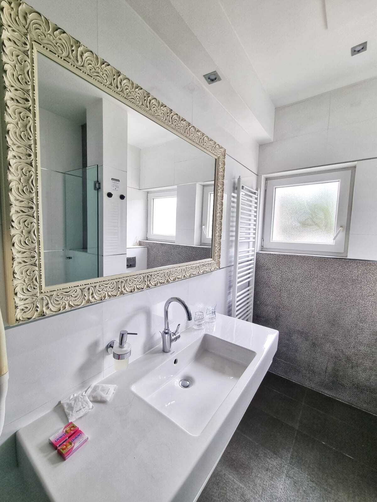 Un bany amb un mirall gran i ornamentat, un lavabo blanc i una finestra.