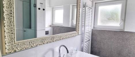 Un bany amb un mirall gran i ornamentat, un lavabo blanc i una finestra.