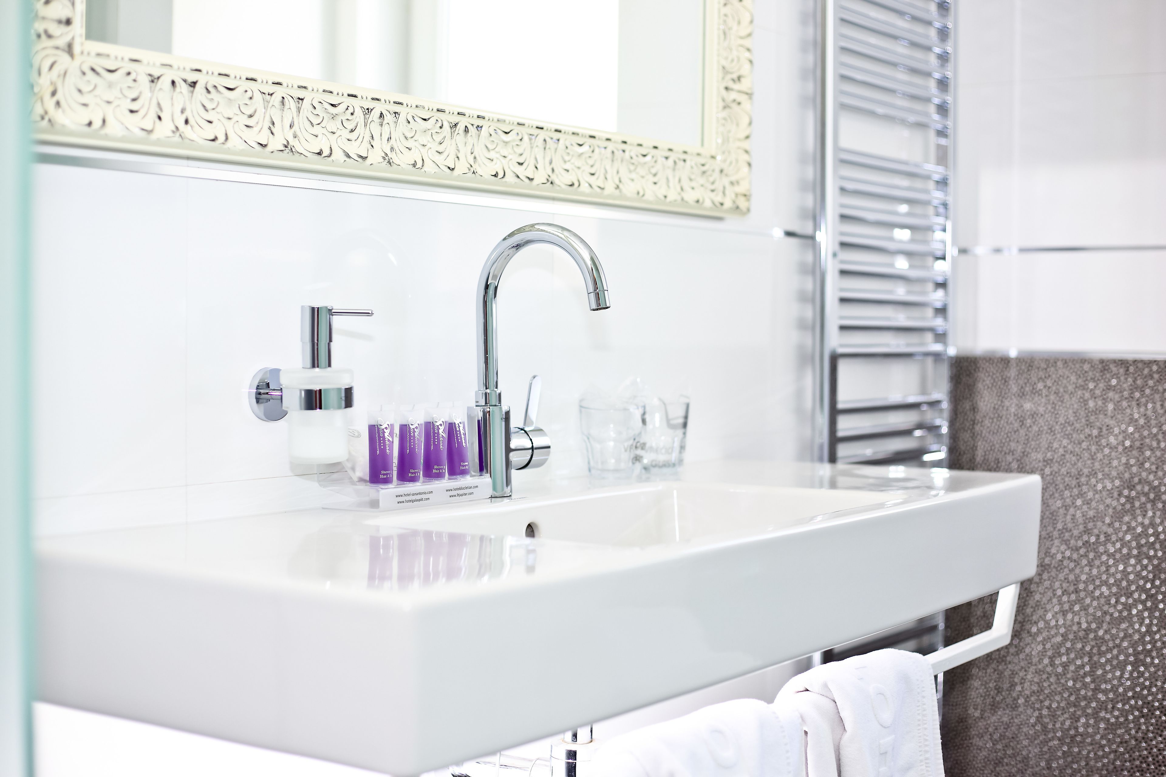 A bathroom with a white sink, a mirror with an ornate frame, and a towel rack with a white towel.