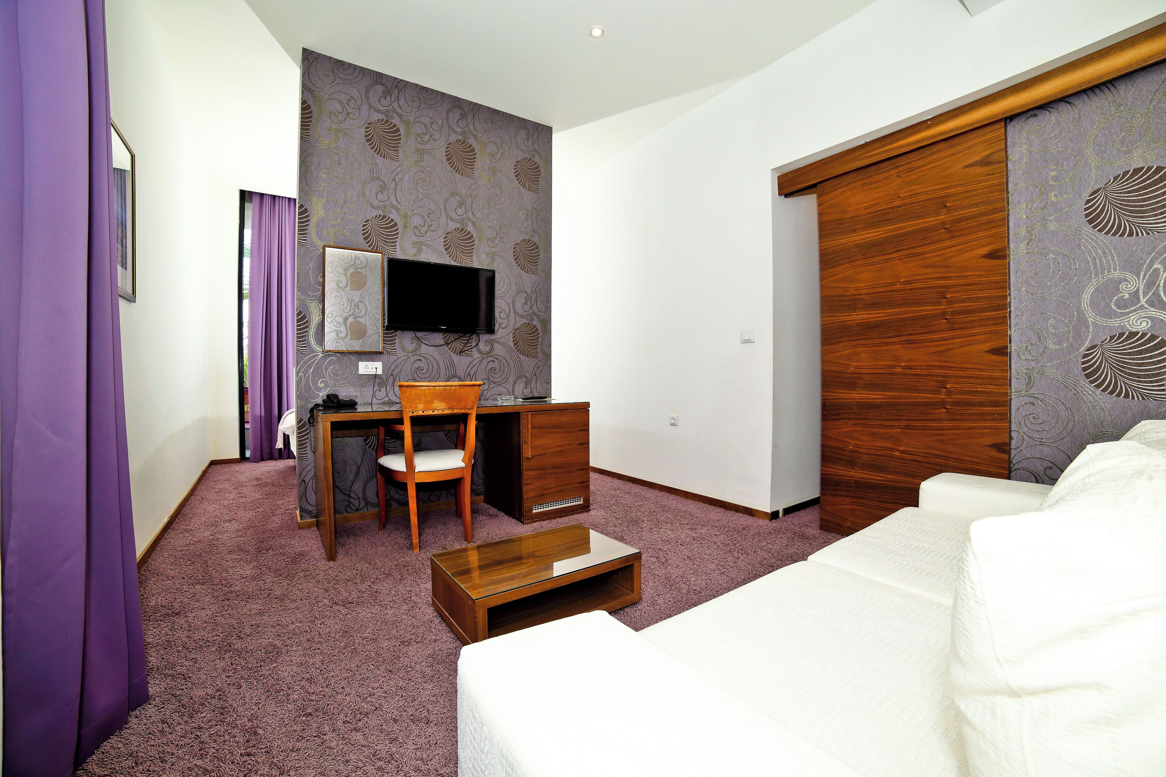A hotel room with a bed, a desk with a chair, a television, and a wardrobe.