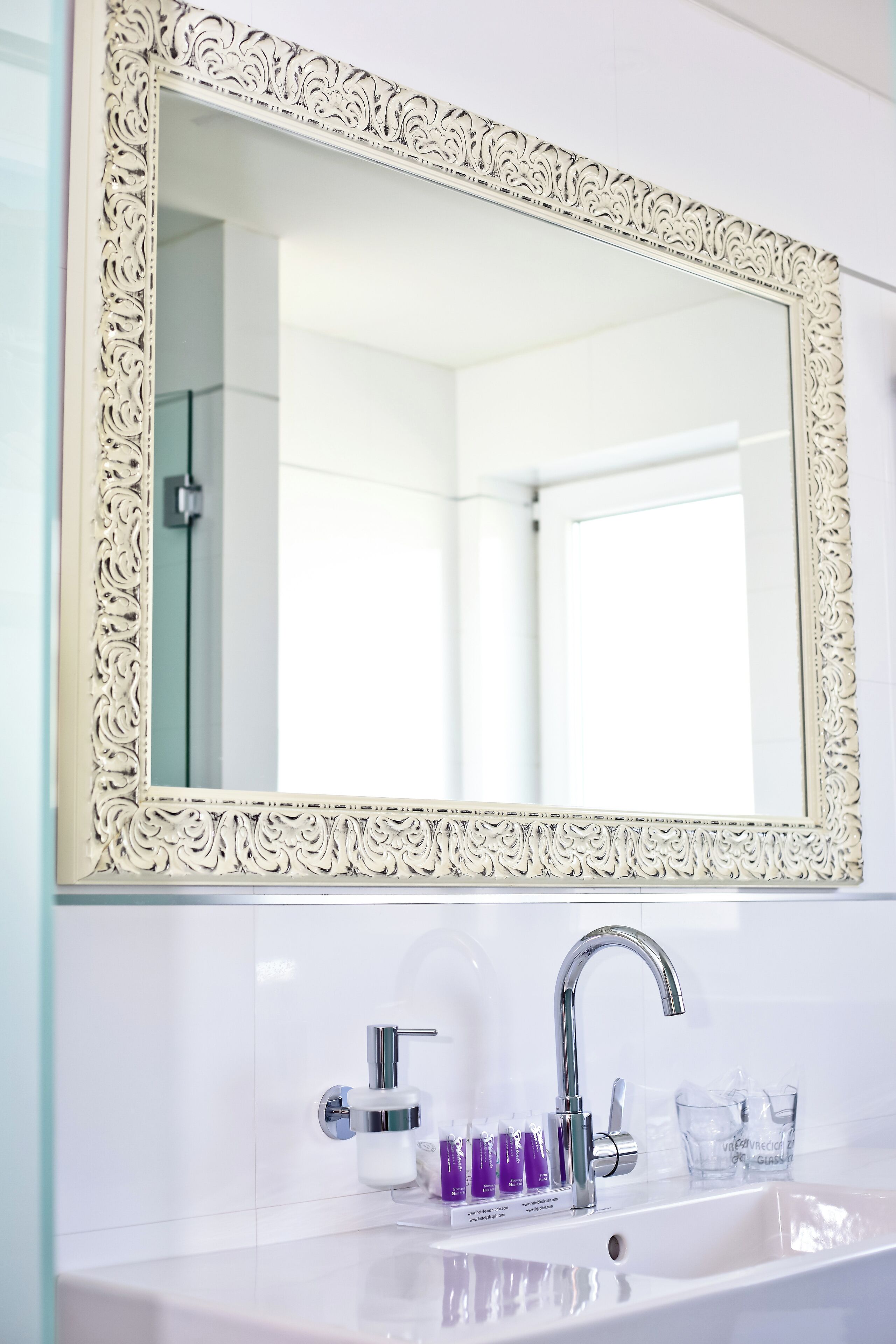 Un baño con un lavamanos blanco, un espejo grande y decorado, y un grifo moderno.