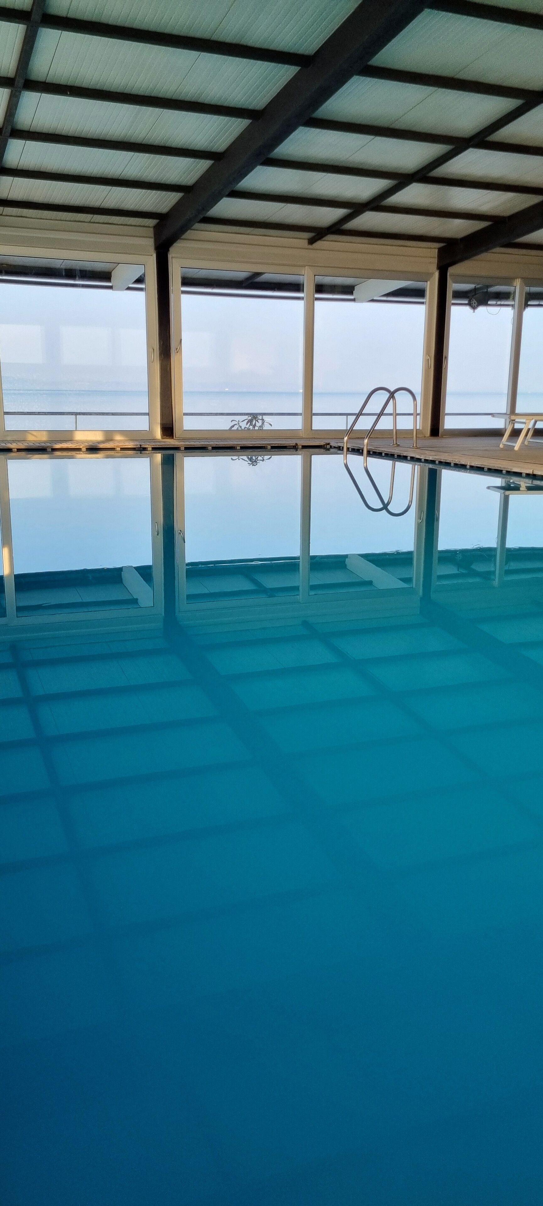 Ein Innenpool mit Infinity-Kante und freiem Blick auf den Ozean, inklusive Metallleiter und Holzterrasse.