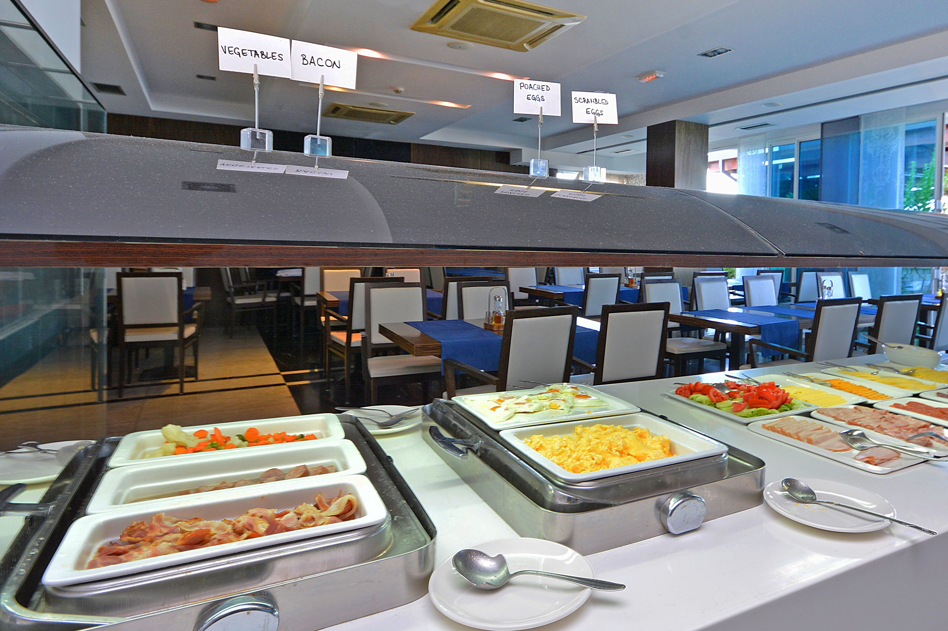 A buffet with labeled sections for vegetables, bacon, poached eggs, and scrambled eggs.
