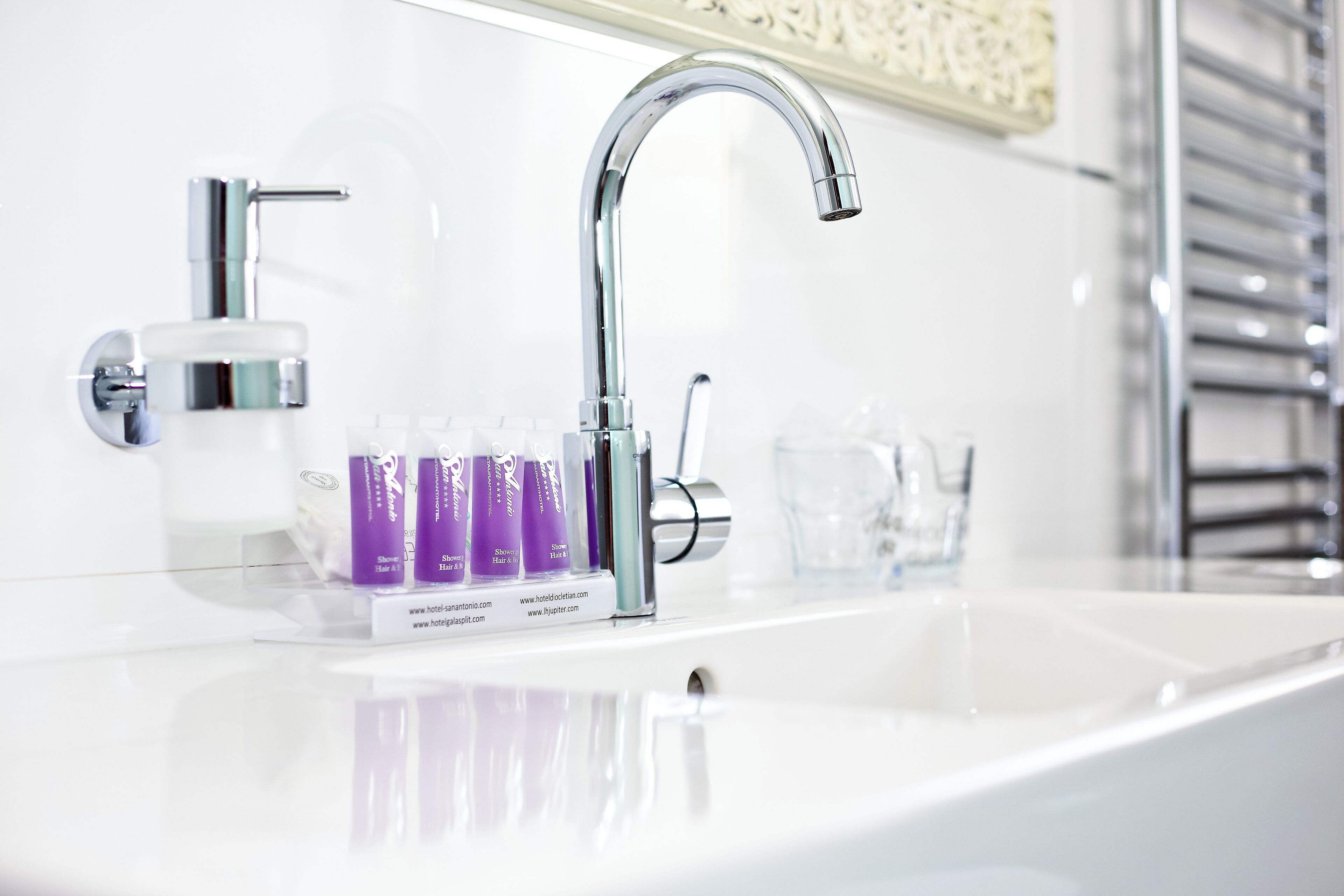 A modern bathroom with a chrome faucet, a soap dispenser, and a row of purple shampoo bottles.