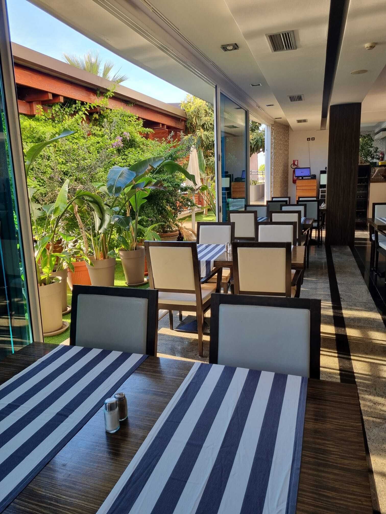 En restaurang med uteservering, krukväxter och utsikt över grönområden.
