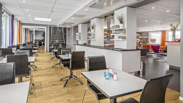 A modern dining area with multiple tables and chairs, a staircase, and a counter with books and plants. - Sure Hotel by Best Western Stockholm Alvsjo (Älvsjö)