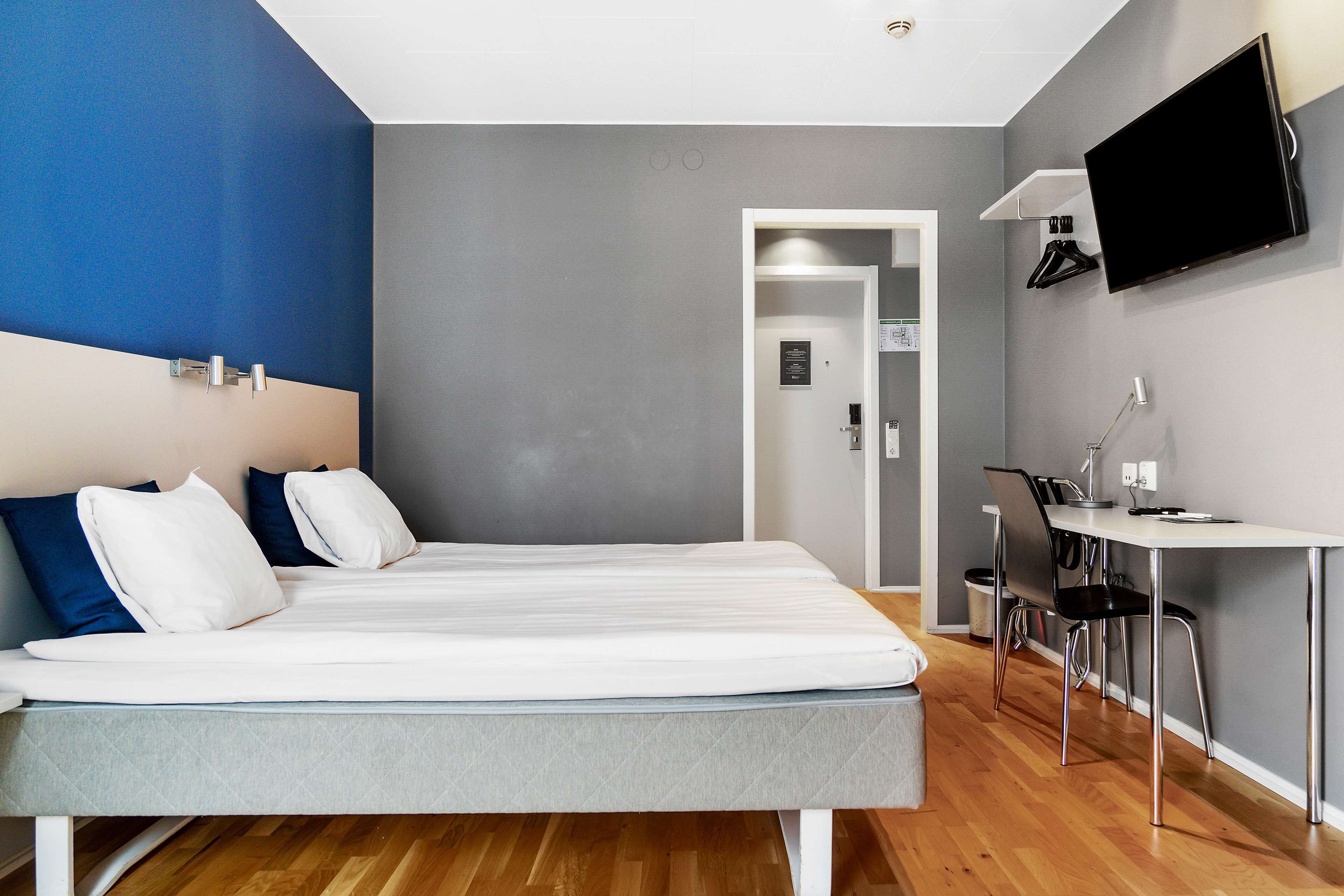Ett modernt hotellrum med en säng, ett skrivbord och en TV.