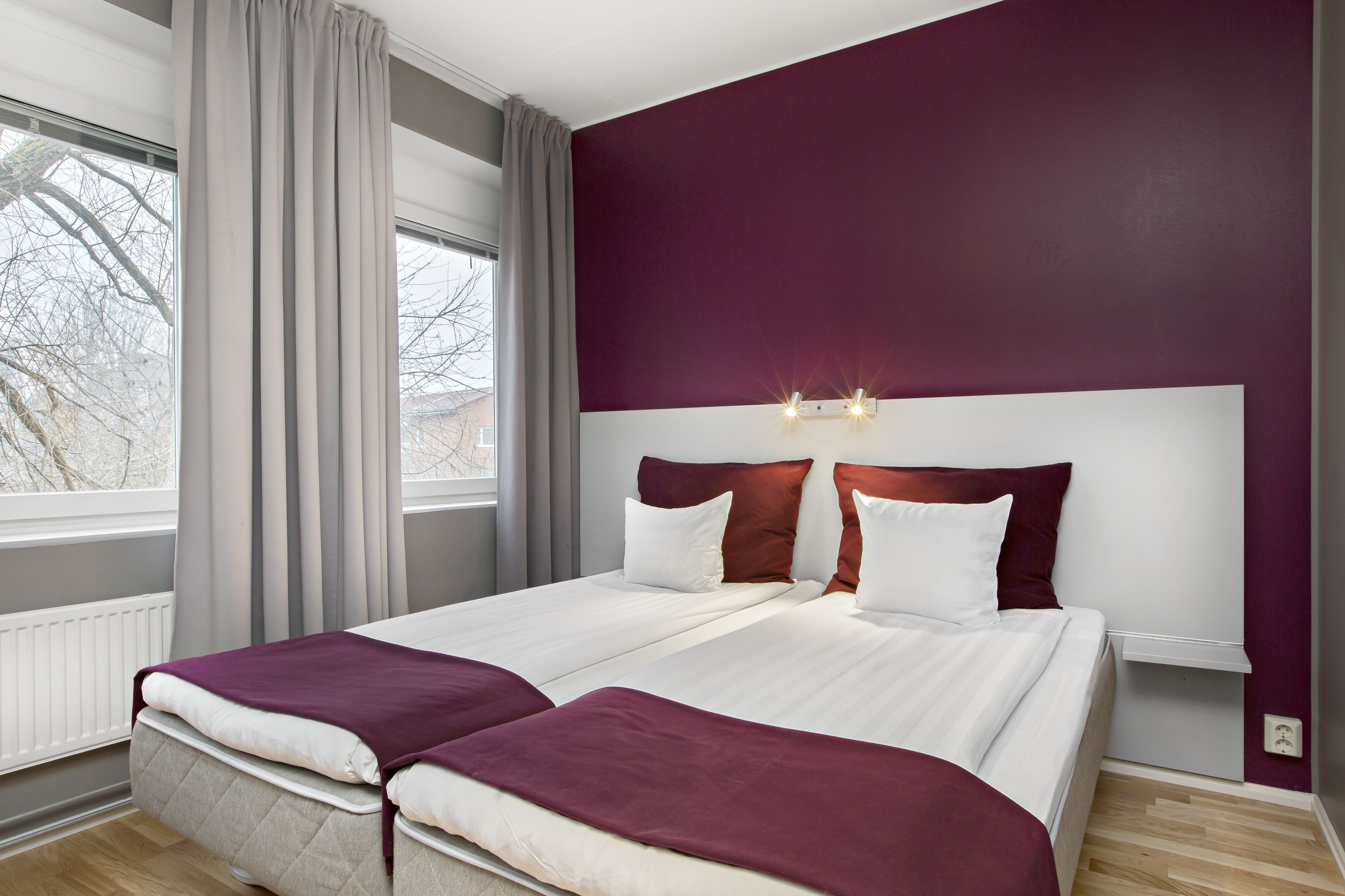 A double bed with a headboard, a window with curtains, and a view of trees outside.