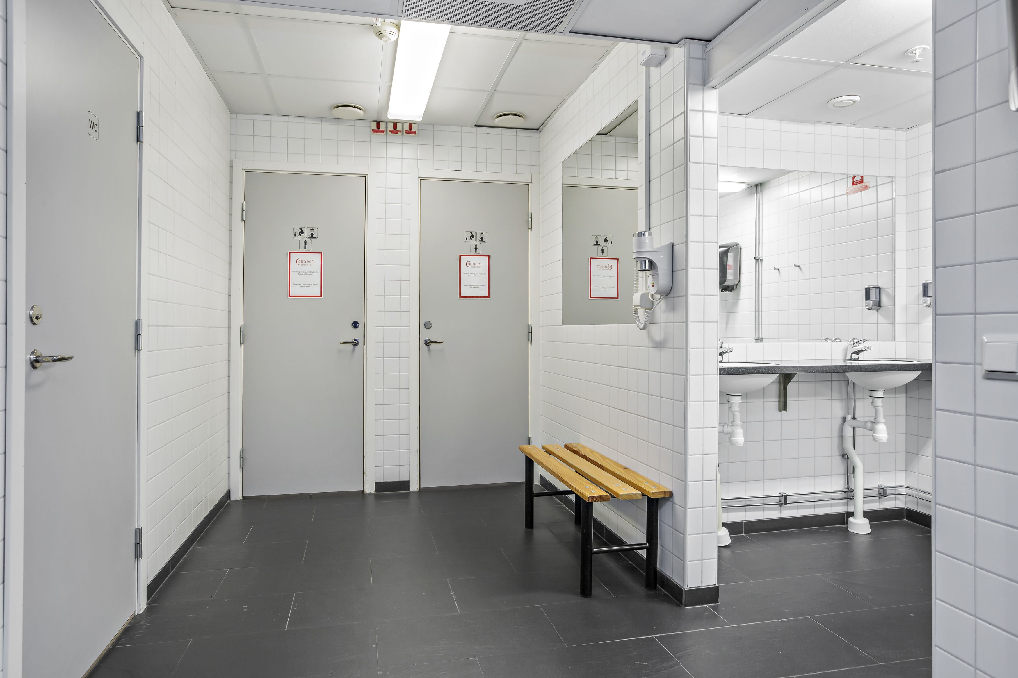 Un baño público con dos puertas, un banco, un espejo y un lavamanos.