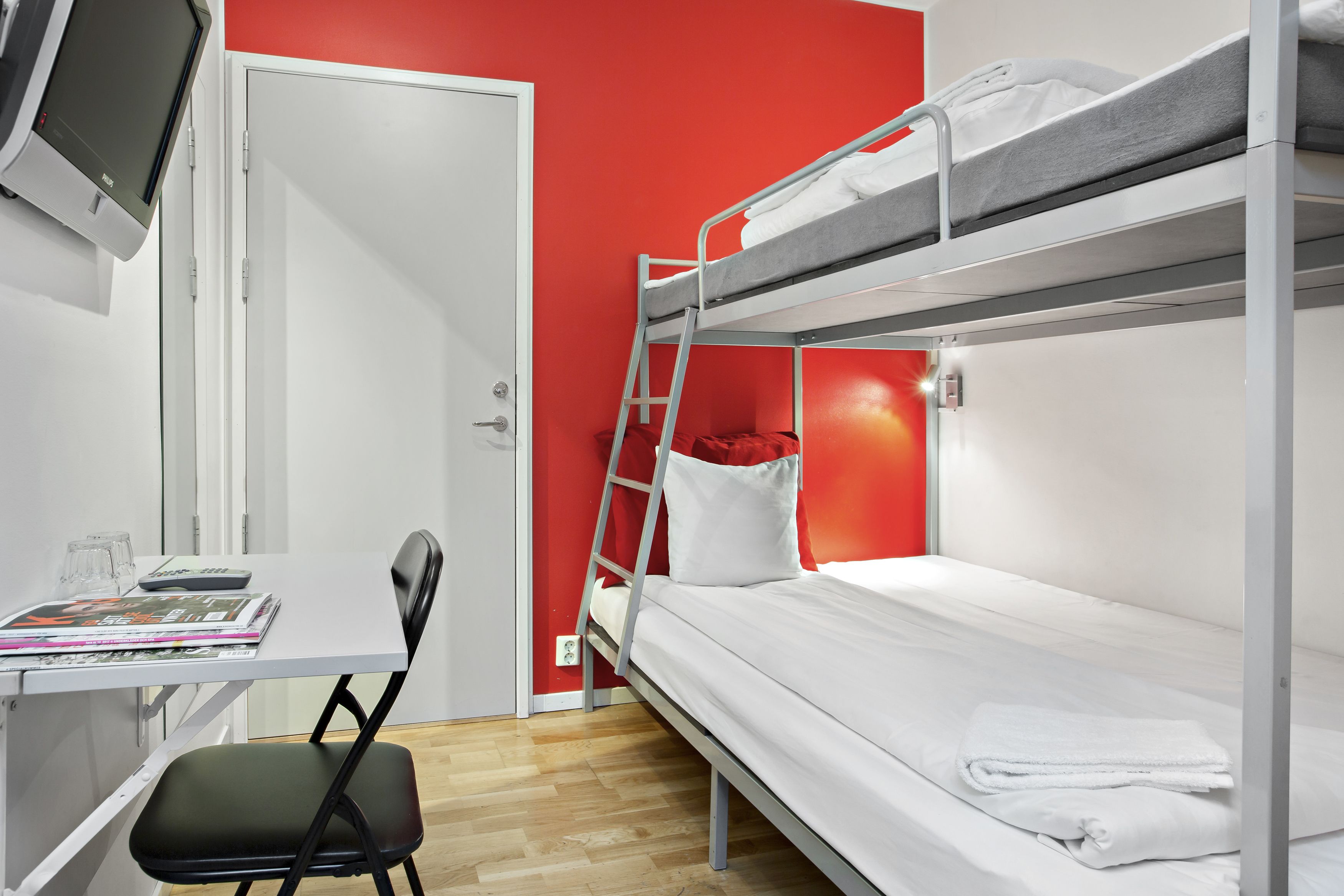 A bunk bed room with a desk, chair, and a television mounted on the wall.