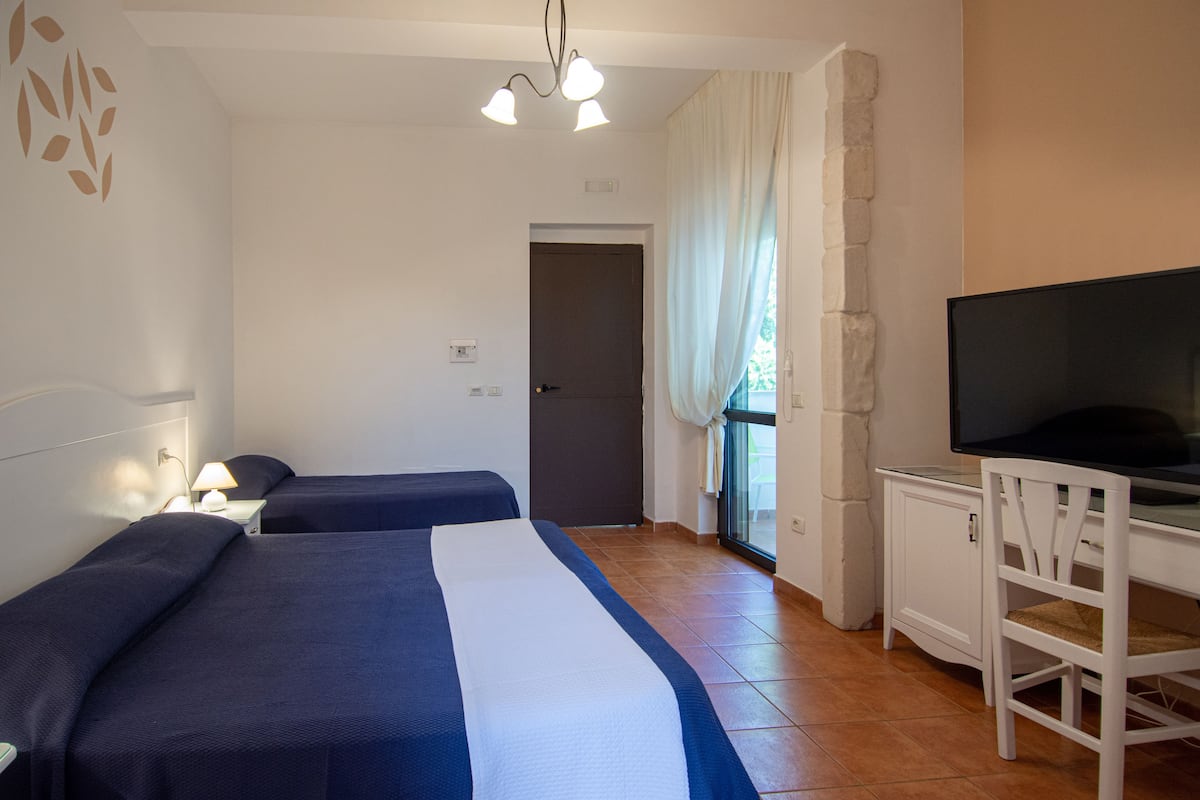 Une chambre d’hôtel avec deux lits, un bureau avec une télévision et une fenêtre avec des rideaux.